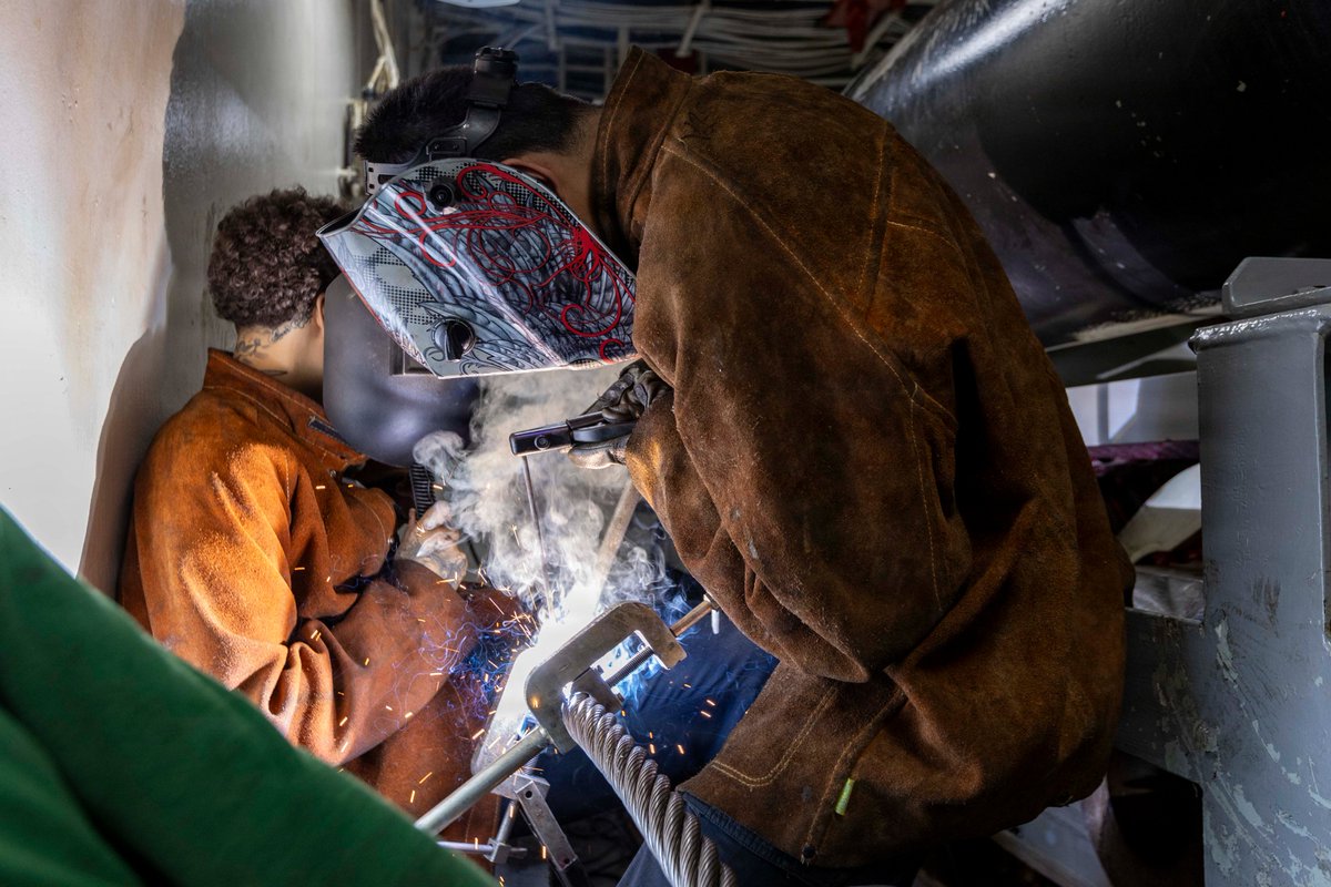 Sailors aboard USS Abraham Lincoln (CVN 72) weld an arresting wire under the flight deck as the carrier strike group operates in the Arabian Sea.