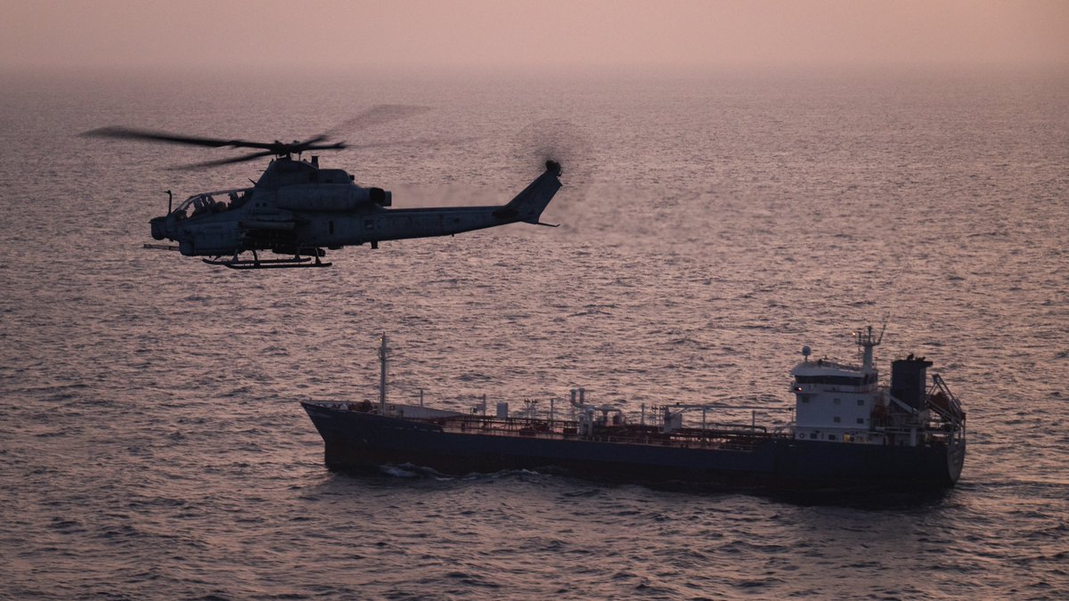 A U.S. Marine Corps AH-1Z Viper attack helicopter patrols near a commercial vessel during enforcement of the maritime blockade against Iran; U.S. forces have redirected 90 ships and disabled 4 as of May 20.