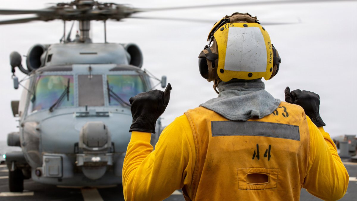 A U.S. Sailor signals to the pilot of an MH-60R Sea Hawk helicopter on the flight deck of USS John Paul Jones (DDG 53) as the guided-missile destroyer continues enforcing the U.S. blockade against Iran. As of Sept. 13, U.S. forces have redirected 101 commercial vessels to ensure
